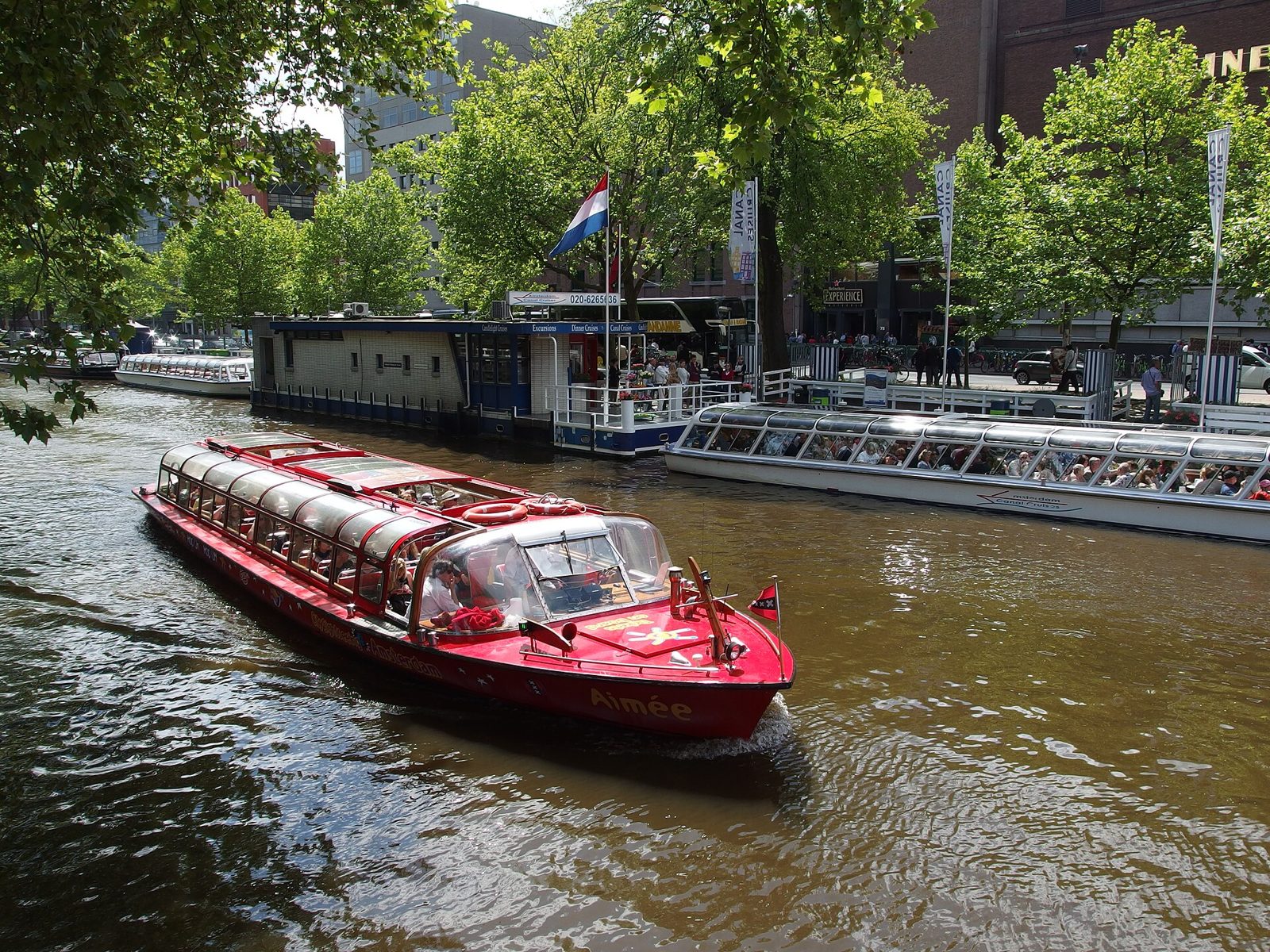Small canal boat on an Amsterdam canal cruise past houseboats